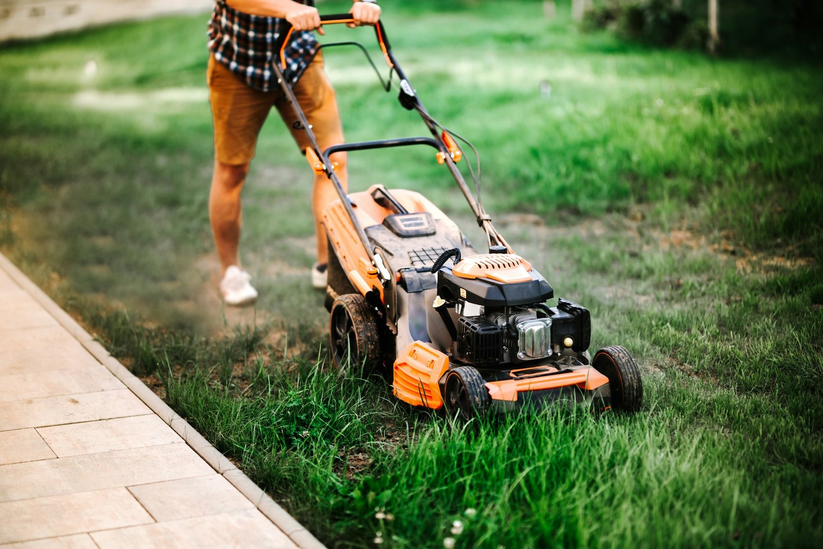 worker, gardener working with lawnmower and cutting grass in garden